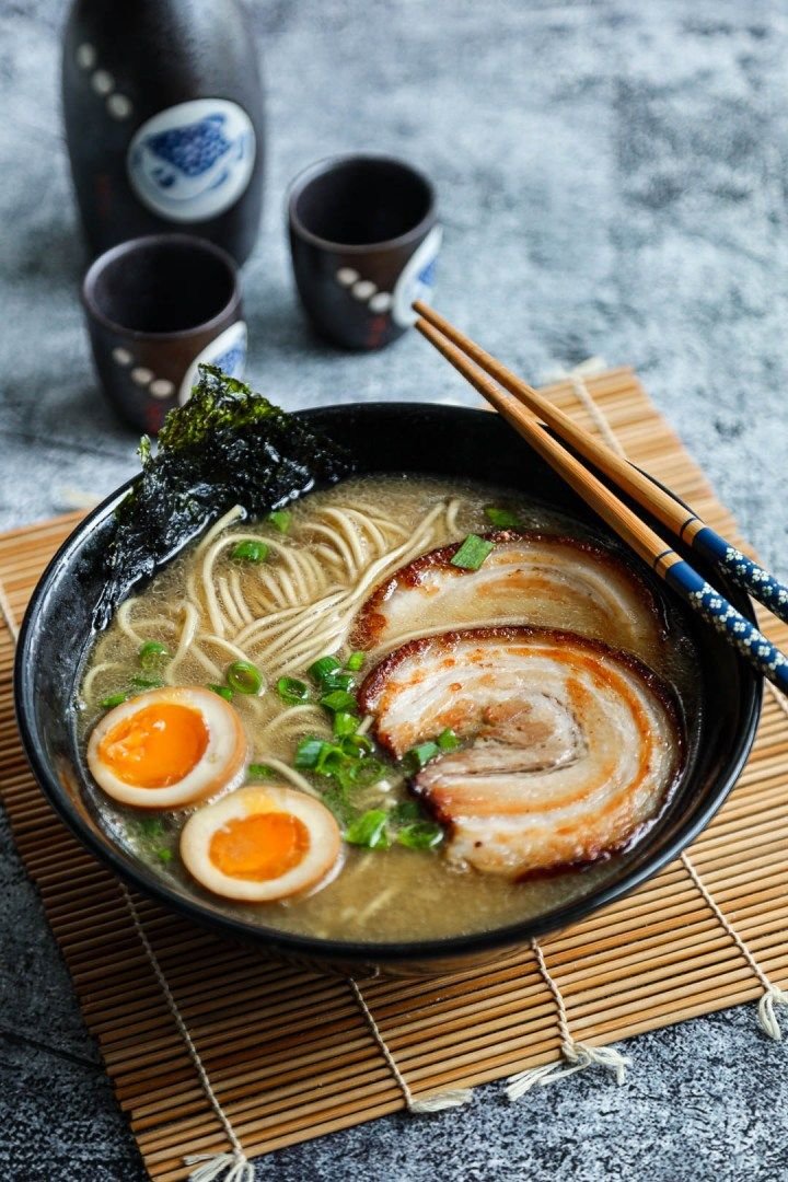 Hands placing toppings on a bowl of ramen